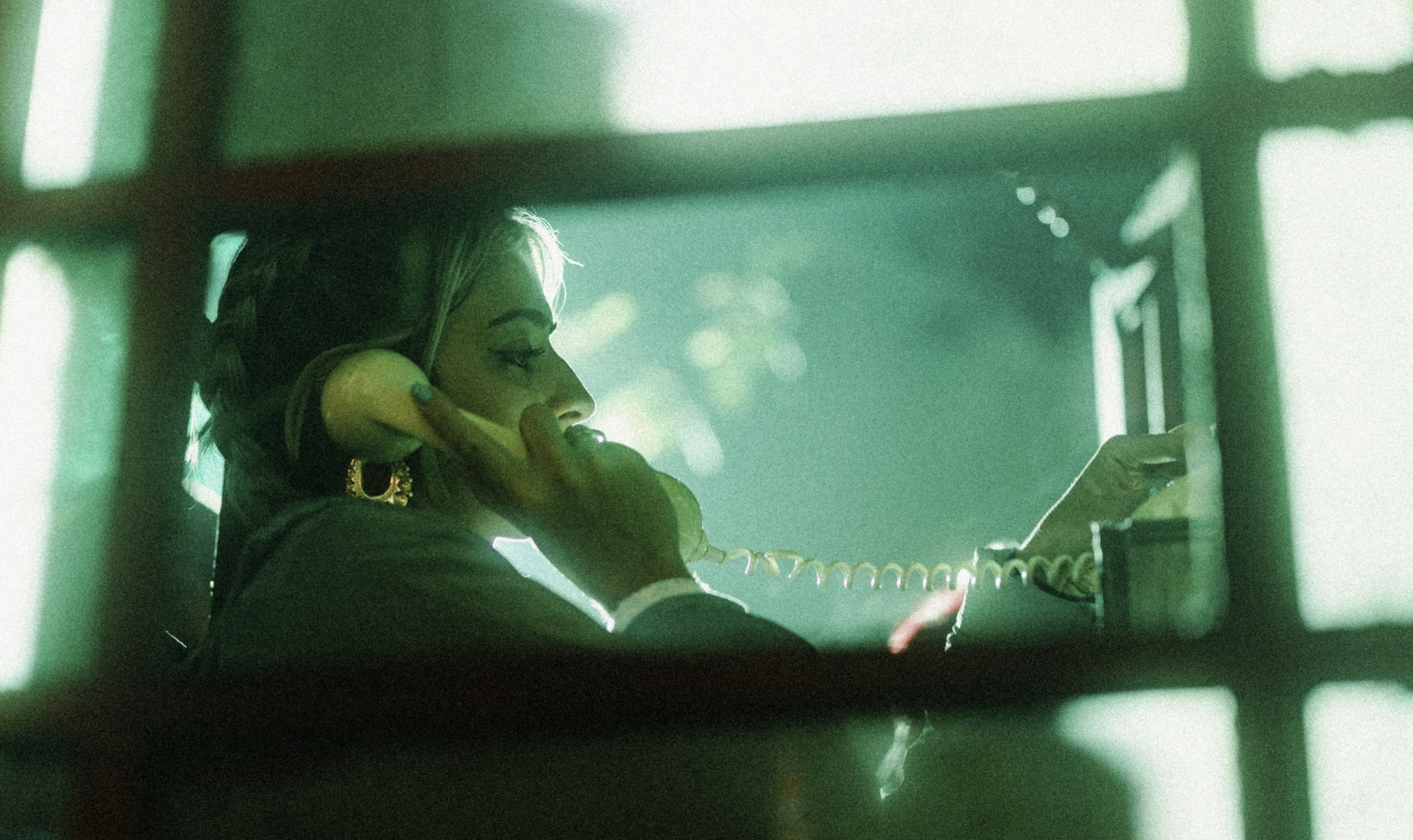 A photograph of a person in an old phone booth, with a phone held to their ear.