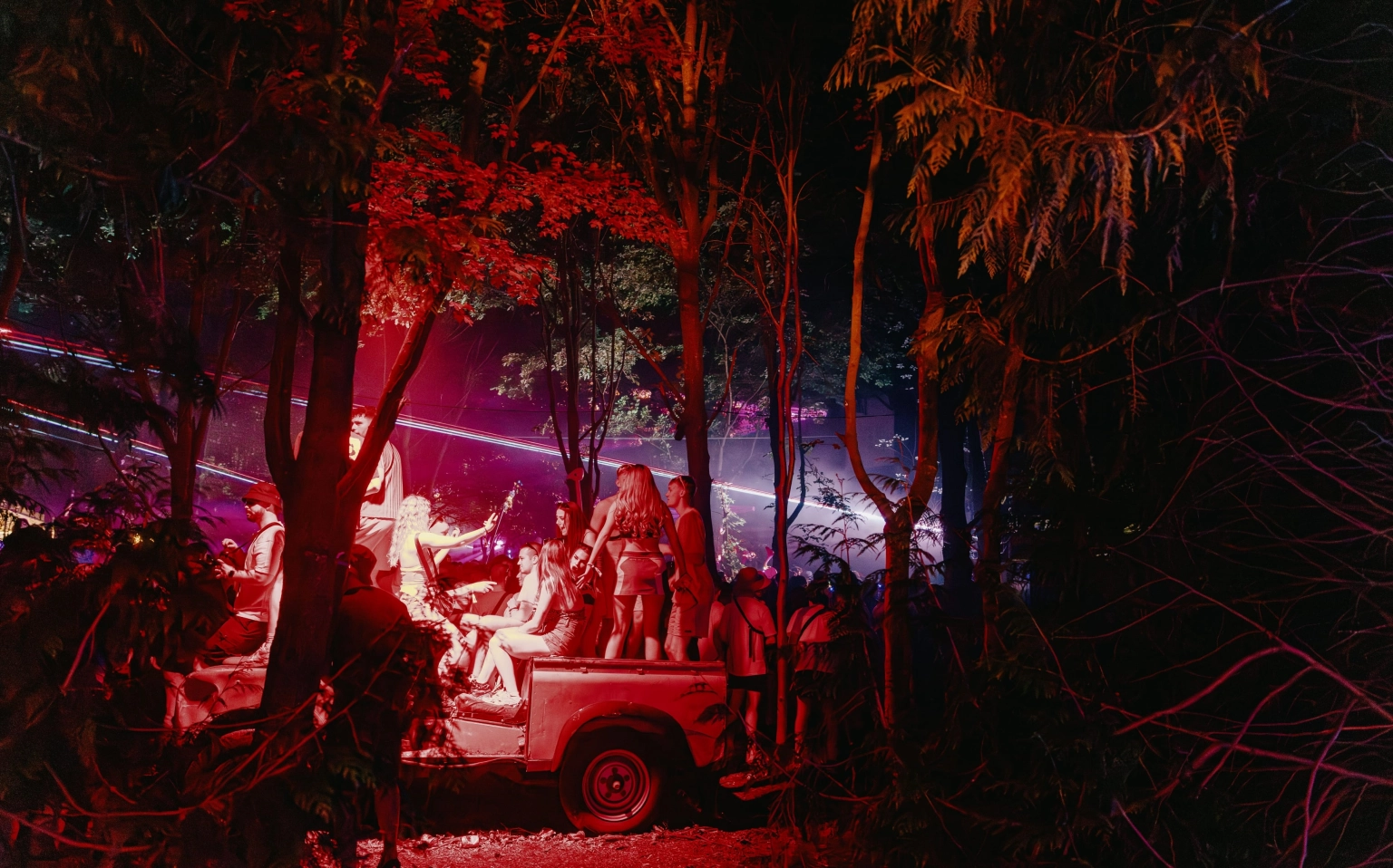 A photograph of revellers at Lost Village, dancing on an old vehicle in the middle of the woods.