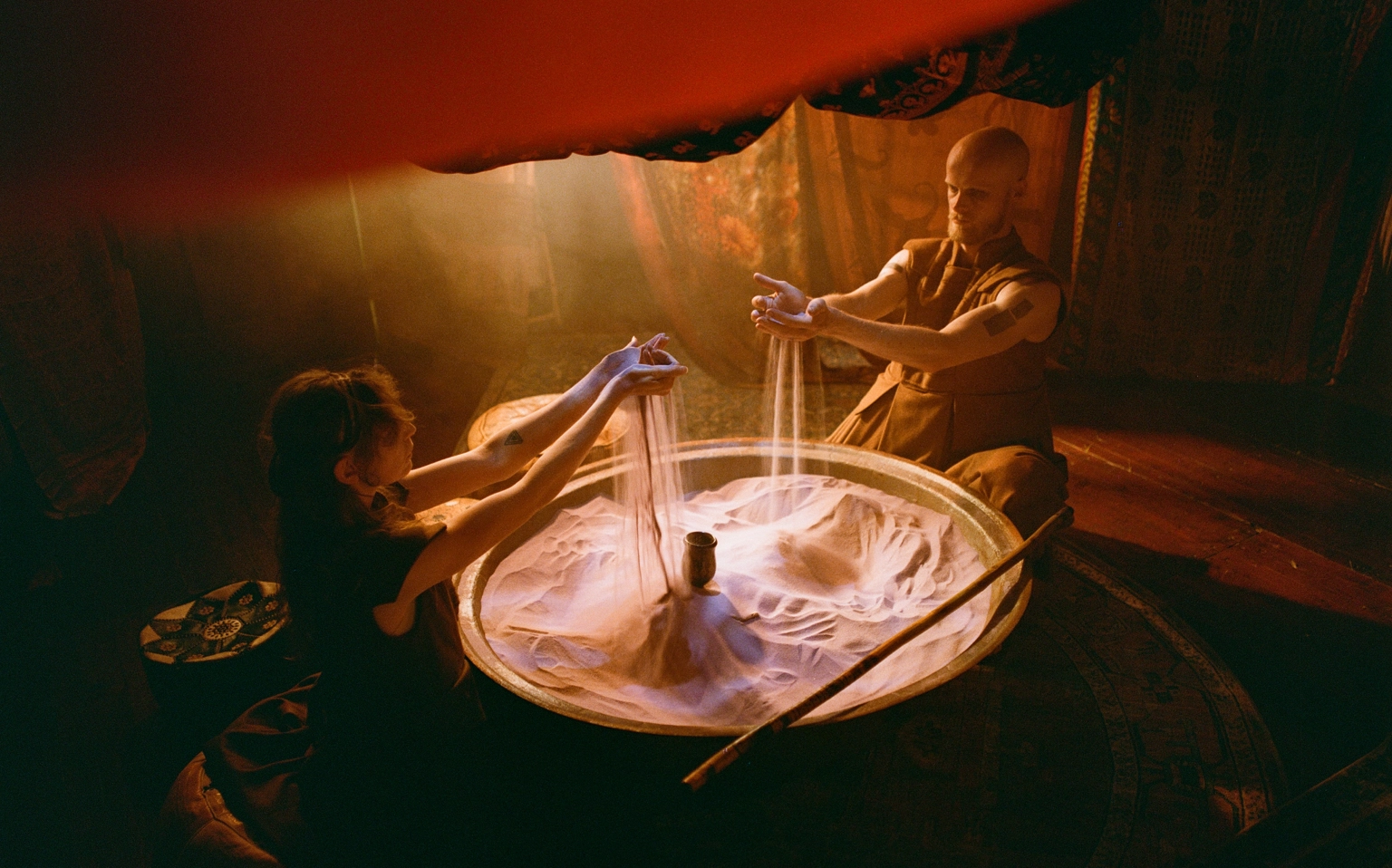 A cinematic photograph of two people performing a ritual with sand at Lost Village.