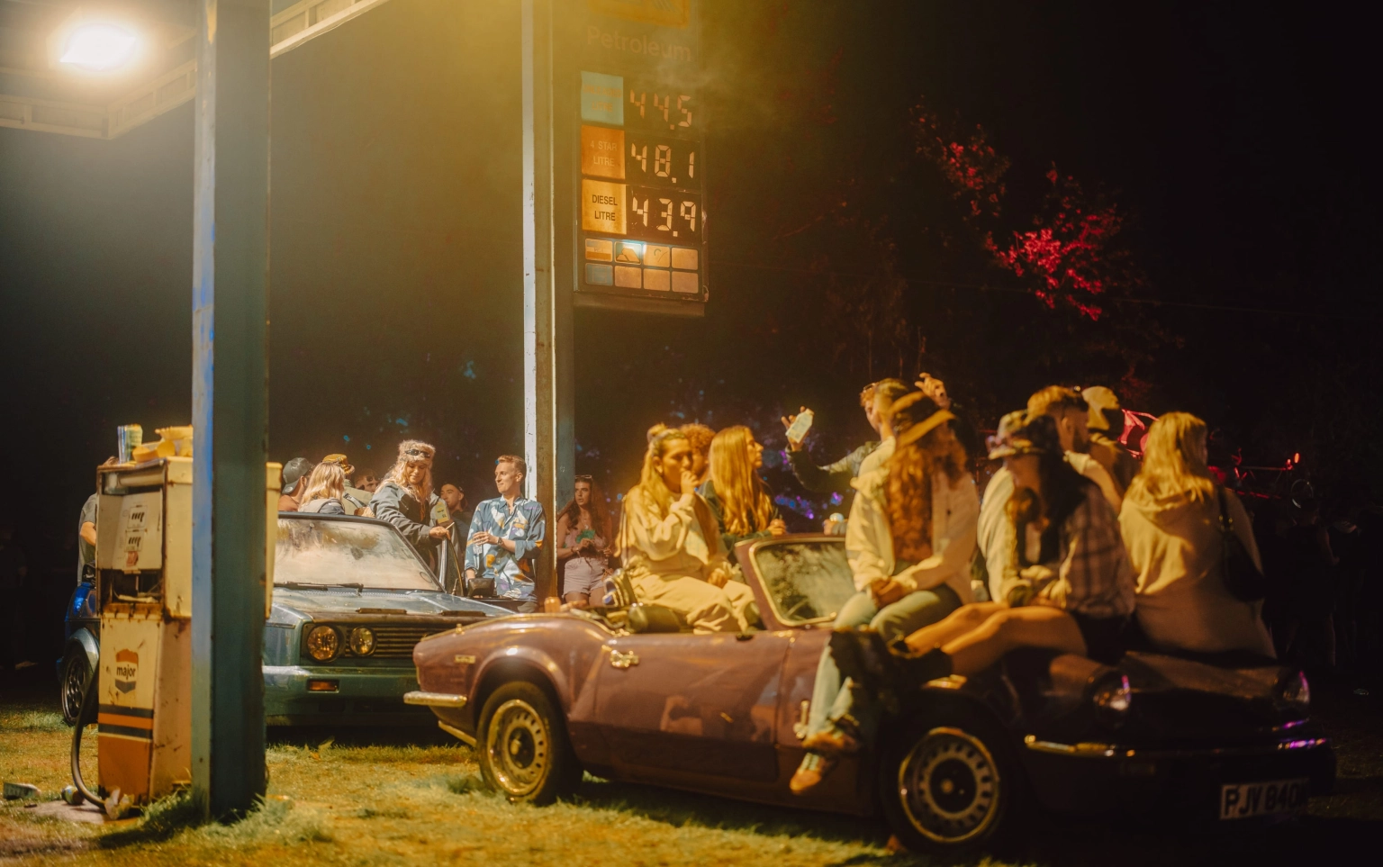 A photograph of people sat on abandoned vintage cars at the gas station set at Lost Village.