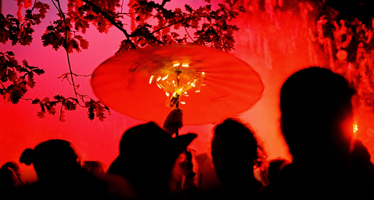 An abstract photograph of silhouetted people twirling a lit parasol at Lost Village.