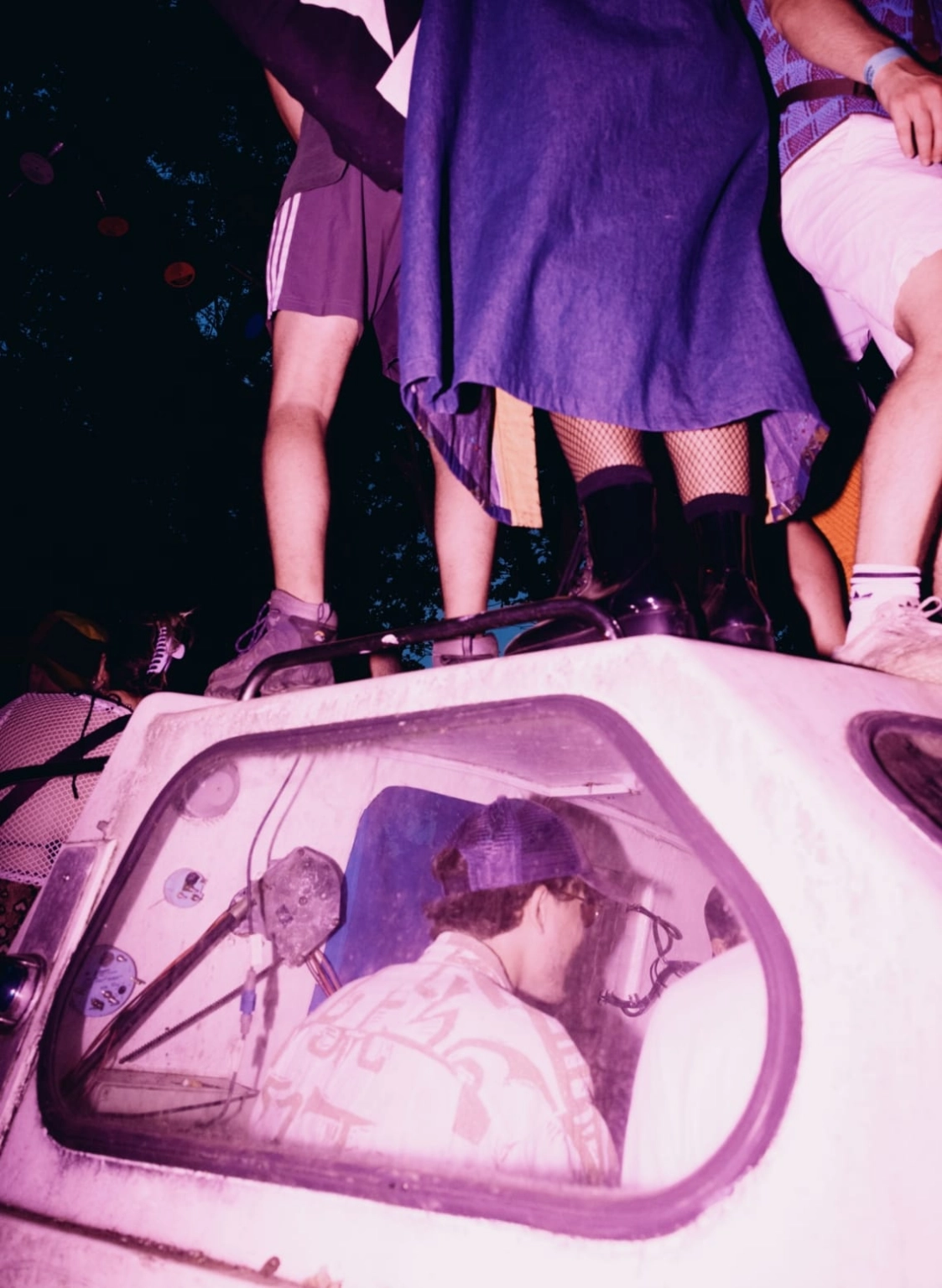 A film photograph of people dancing on a vehicle, with people sat inside the vehicle.