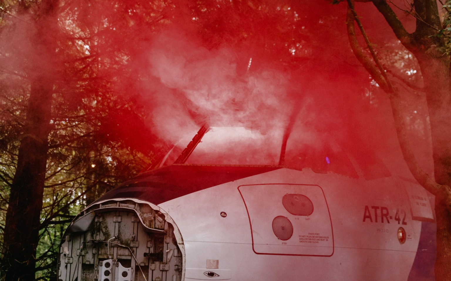 A cinematic photograph of the Airbase at Lost Village, featuring a broken plane with red smoke emanating from it.
