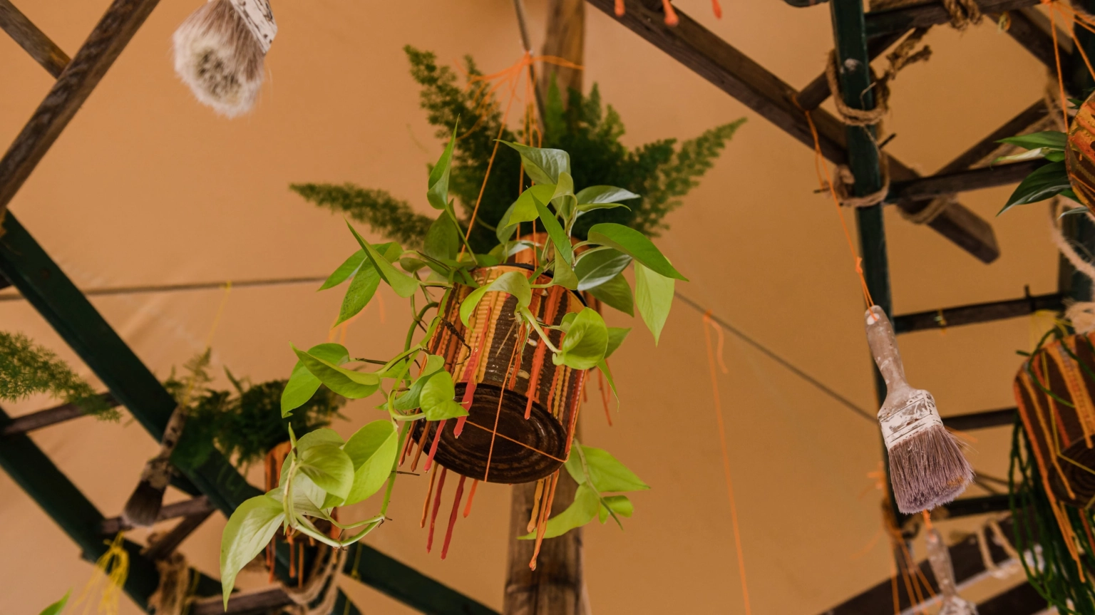 A green plant in a metal container hanging from wooden beams in a tent at Lost Village.